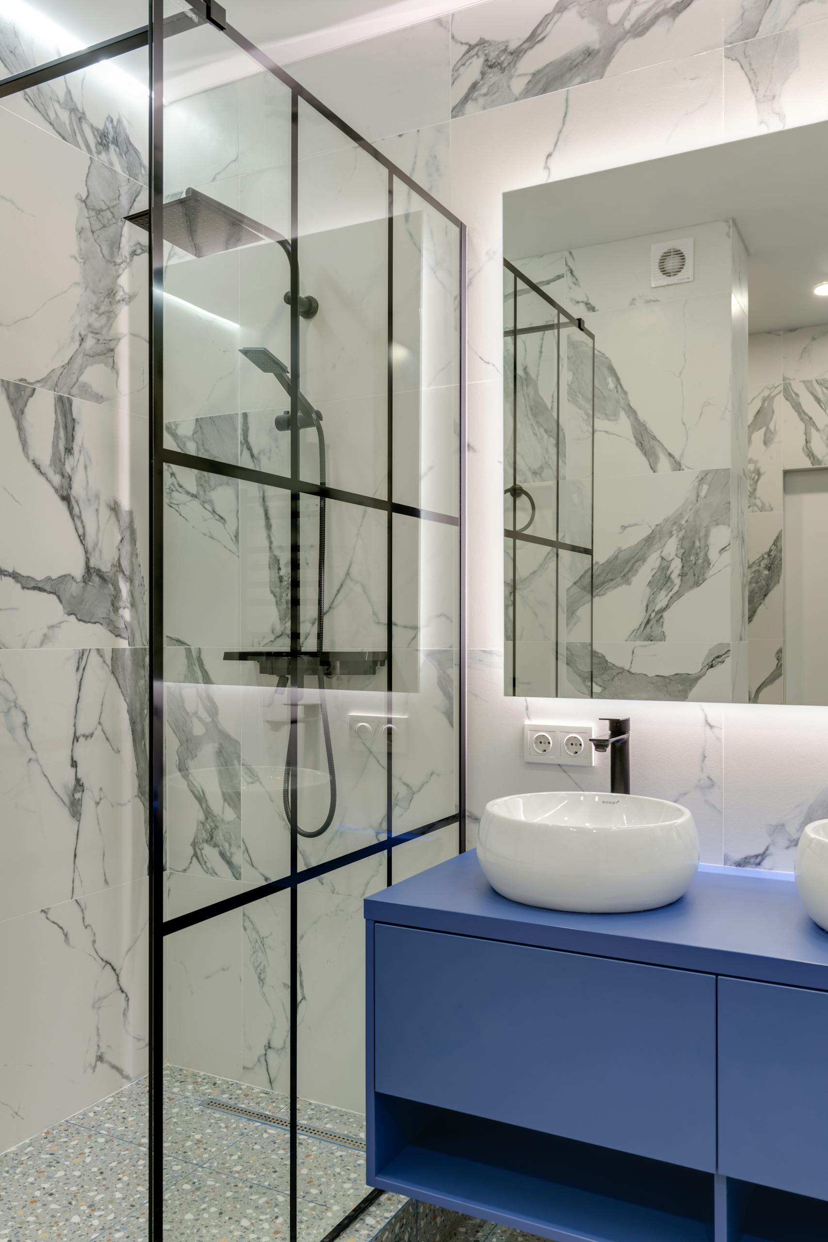 Elegant bathroom featuring a blue vanity, marble tiles, and glass shower enclosure.